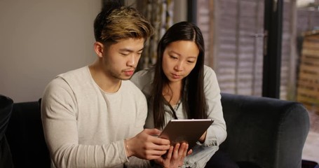 4K Young serious couple looking at computer tablet together at home