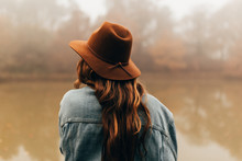 Rear view of woman in hat standing by pond on foggy day