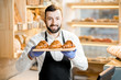 © rh2010 - Portrait of a handsome seller in uniform standing with delicious croissants in the store with bakery products