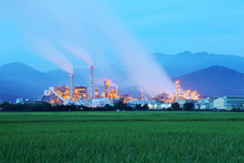 View Of A Factory In The Middle Of A Green Farmland In The Early Morning Twilight ~ Factory Pipes Polluting Air In A Silent Morning, A Serious Environmental Issue