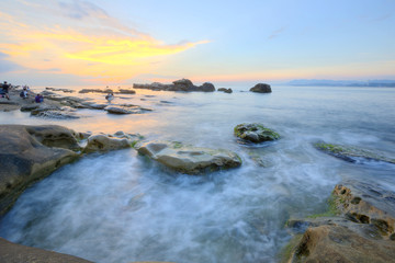 Wall Mural - Dramatic dawning sky with golden clouds over the rocky coast ~ Scenery of rising sun illuminating the sea water at a rocky beach ( Long Exposure Effect )