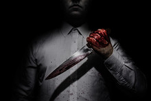 Photo Of A Killer In White Shirt Holding A Bloody Knife On Black Background With Upper Lighting.