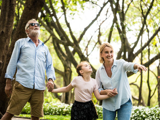 Wall Mural - Happy family having fun together in the garden. Father, mother and daughter holding hands and walking in a park. Lifestyle concept