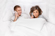 © Denys Kurbatov - Concentrated young woman and funny man lying in bed and talking on phones