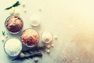 Mix of different salt types on grey concrete background. Sea salts, black and pink Himalayan salt crystals, powder, rosemary. Salt crystal balls from Dead sea. Copy space. Top view.