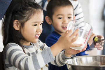 Wall Mural - 計量カップの小麦粉をボウルに流し込む女の子。弟も楽しそう。料理のお手伝い。