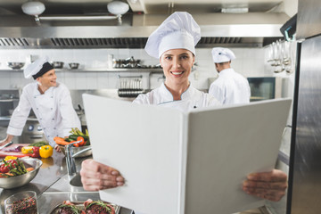 Wall Mural - happy chef holding recipe book at restaurant kitchen