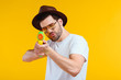 © LIGHTFIELD STUDIOS - bearded young man in hat and sunglasses shooting with water gun isolated on yellow