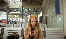 Young Woman Using Her Mobile Phone At Bus Stop