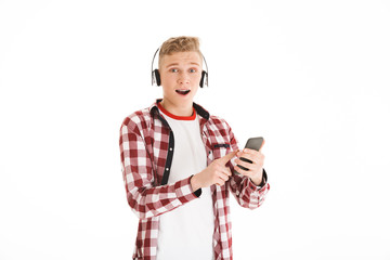 Wall Mural - Modern youngster in casual t-shirt 17y wearing braces listening to favorite music via wireless earphones and using smartphone, isolated over white background