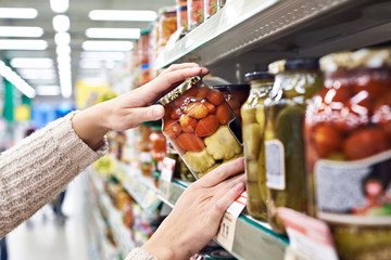 Buyer hands with jar of salted tomatoes and squash in store