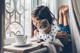 Child relaxing with a cat on a window sill
