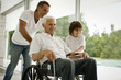 © Erickson Stock - Senior man being pushed in wheelchair,  by his adult son and his grandson.