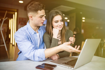 Sticker - Happy young couple is using a laptop, drinking coffee and smiling while sitting at the cafe