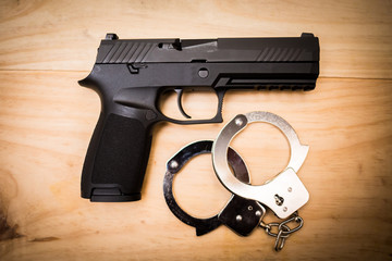 Wall Mural - Hand gun with hand cuffs on wooden surface