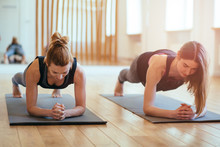 Front View Of Two Sporty Fit And Slim Middle Aged Women Doing Planking Exercise Indoors Together With A Natural Light In Modern Interior Sport Studio Hall Or Yoga Class.