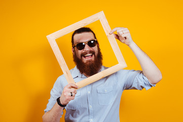 Smiling bearded hipster man in casual with sunglasses into a wooden frame