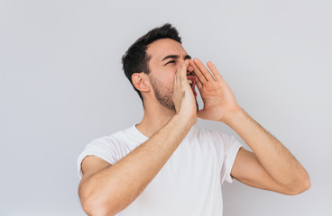 Sticker - Handsome aggressive male opens mouth widely, screams in panic with hands on mouth, being in stressful situation posing over white studio wall background. People and emotion concept.