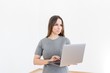 © pantovich - Woman in gray dress standing with laptop in hands on white background