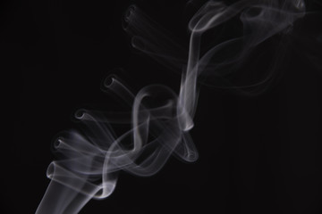 Smoke from an incense stick, which forms strange shapes, on a black background. 