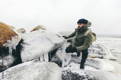 Man crouching by frozen rocks at beach