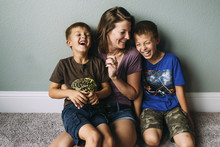Cheerful Mother And Sons Sitting Against Wall At Home