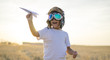Kid, Little boy wearing helmet and dreams of becoming an aviator while playing a paper plane at sunset