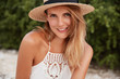 © WHstudio Leushin N - Outdoor shot of happy delighted female with pleasant look, wears summer white dress and hat, poses against green vegetation background, being in good mood. People, emotions and rest concept.