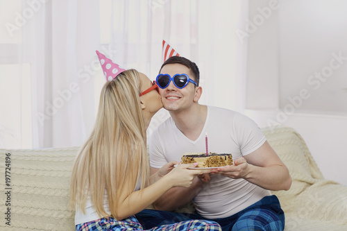 Zdjęcie XXL Para z tortem ze świeczkami gratuluje na urodziny na tle okna w pokoju.