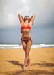 © Lubo Ivanko - Young woman in red swimsuit and sunglasses, standing on the beach holding her hands behind head, looking up into the sun. Kalutara beach, Sri Lanka