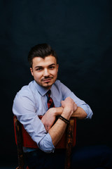 Portrait of young man in casual dressed in shirt and tie sitting on chair with crossed arms