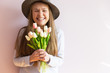 © AnastazjaSoroka - A young beautiful girl with blond dissolved long hair, a felt hat on her head, keeps spring flowers in her hands on a sunny day. Women's Day.