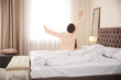 © New Africa - Young woman stretching on bed in hotel room