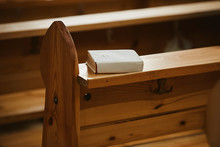 Holy Bible In A White Paper Cover On A Wooden Bench In Church