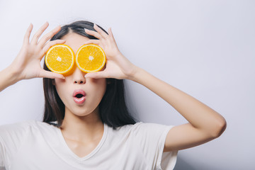 Studio portrait of young surprised funny girl holding two orange slices in t-shirt on white background and smiling. Fresh fruits and healthy diet concept. Free copy space provided