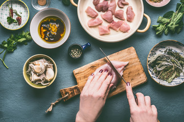 Wall Mural - Chicken meal cooking concept. Female hands cutting chicken breast meat on kitchen tables background with bowls , oil , soy sauce and ingredients, top view