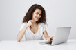 © Cookie Studio - Having great day, enjoying using new laptop. Indoor shot of pleased carefree european woman biting rim of glasses and smiling broadly while looking at screen and typing message in notebook