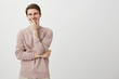 Portrait of positive charming european male covering mouth with hand while laughing and looking aside, standing over gray background. Guy is touched with sense of humour of girl he likes