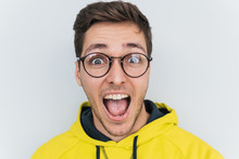 Closeup Portrait Of Amazed Young Caucasian Man Wearing Trendy Glasses And Hoodie, Keeping Mouth Wide Open, Looking Shocked Isolated Over White Studio Background. People, Lifestyle And Emotion Concept.