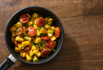 Wall Mural - Roasted Potato and Sausage in frying pan on wooden table. Top view with copy space