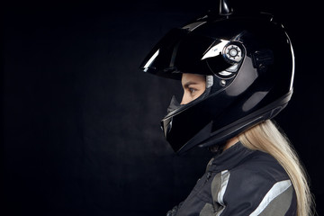 Profile portrait of fashionable young European woman rider with blonde hair preparing for motor race standing isolated wearing new black motorcycle safety helmet, having focused determined look