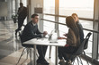 © Yakobchuk Olena - Two women and male sitting at table in spacious office and talking. African male with cellphone standing on background