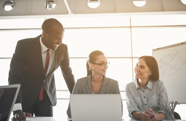 Two women and man communicating with satisfaction while sitting in meeting room with devices