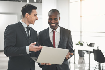 Waist up of caucasian and african male people standing with notebook and conversing
