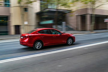 Red car in motion on the road, Sydney, Australia. Car moving on the road, blurred buildings in background.