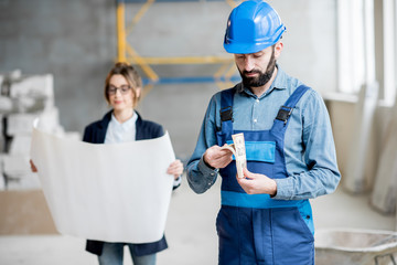 Builder counting money standing at the construction site with woman customer on the background