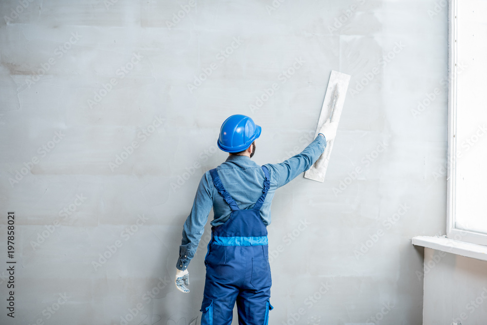 Plasterer in blue working uniform plastering the wall indoors - obrazy, fototapety, plakaty 