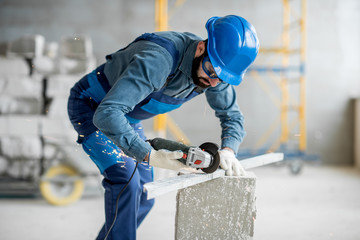 Builder in working uniform cutting metal profile with cutting machine at the construction site indoors