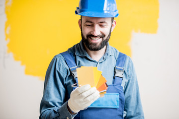 Wall Mural - Painter in blue workwear holding color swatches on the yellow wall background indoors