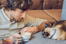 Portrait Of Handsome Young Man Playing With Cat And Drinks Coffee